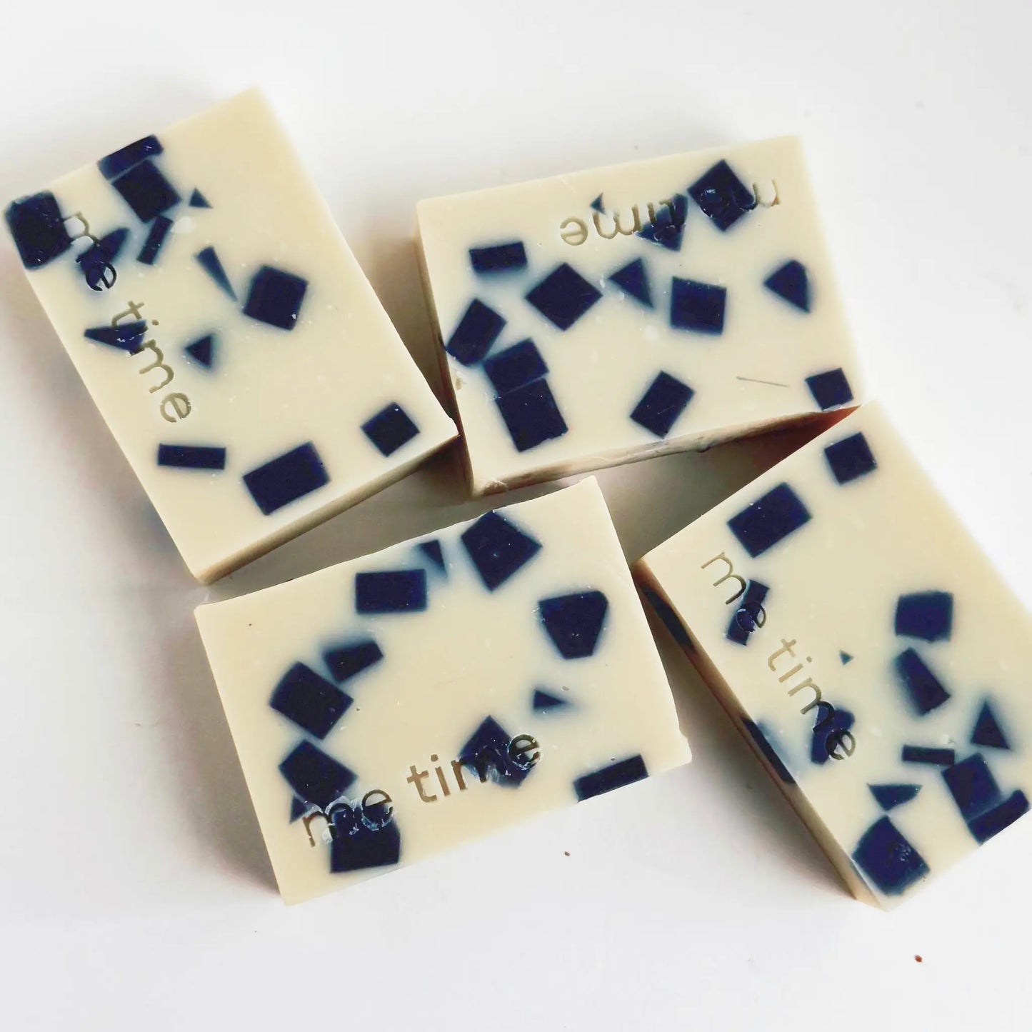 Four soap bars with blue and black square patterns on a white background