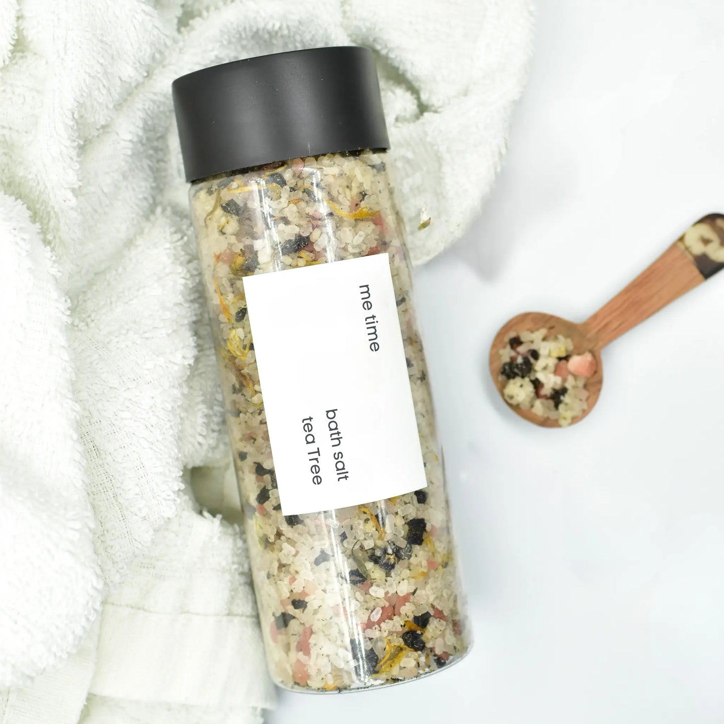 Bottle of bath salts labeled 'me time' with a wooden spoon on a white background