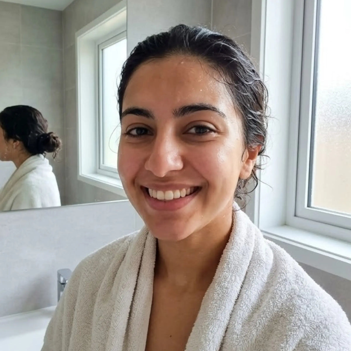 Woman in a white robe smiling in a bathroom after using me time Turmeric Brightening Face Dry Mask
