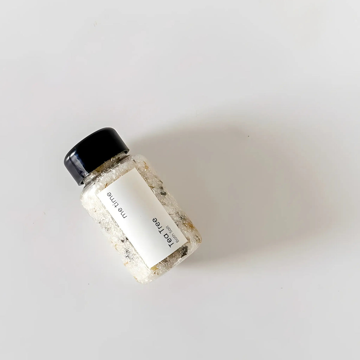 Small bottle of bath salts with a black lid on a light gray background