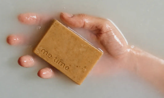 Hand holding a handmade Me Time soap bar submerged in bath water, "me time" engraved on the bar