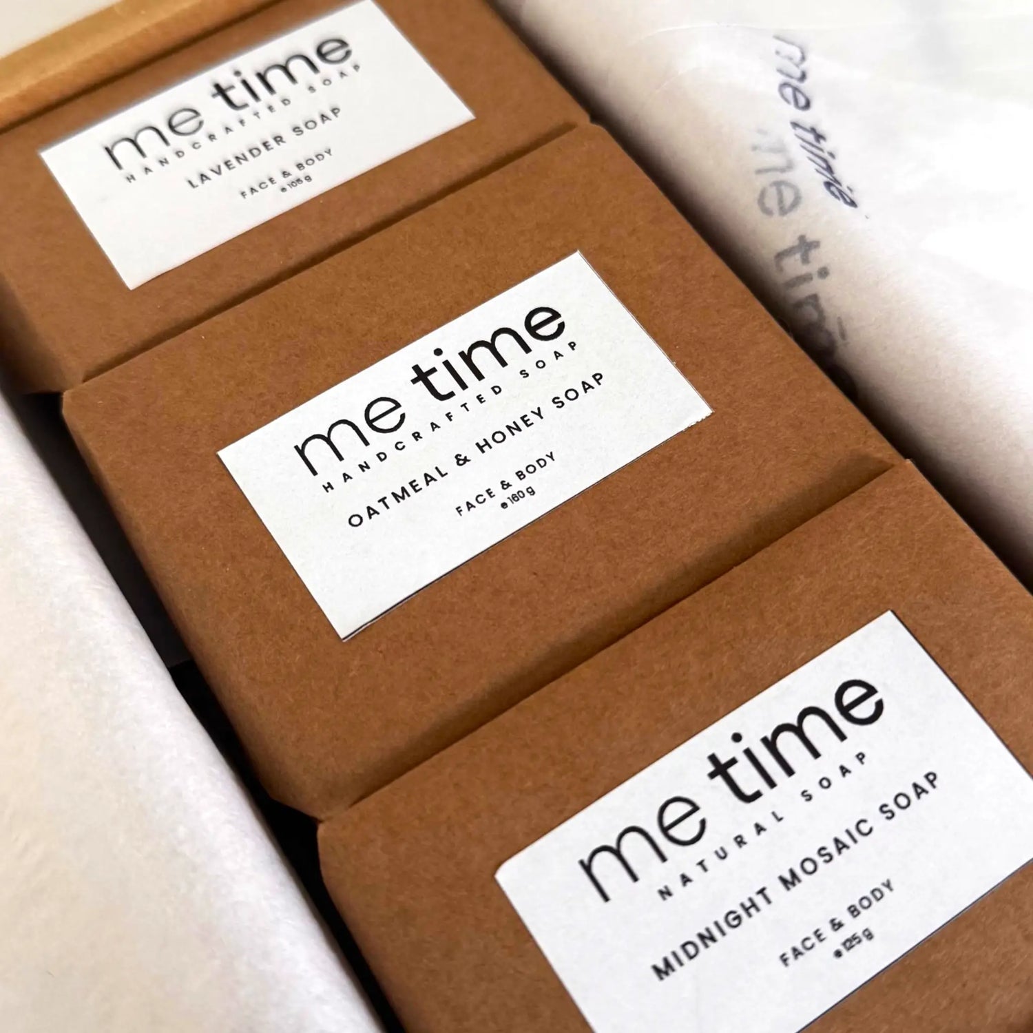 Three 'me time' soap bars in brown packaging with labels on a light background