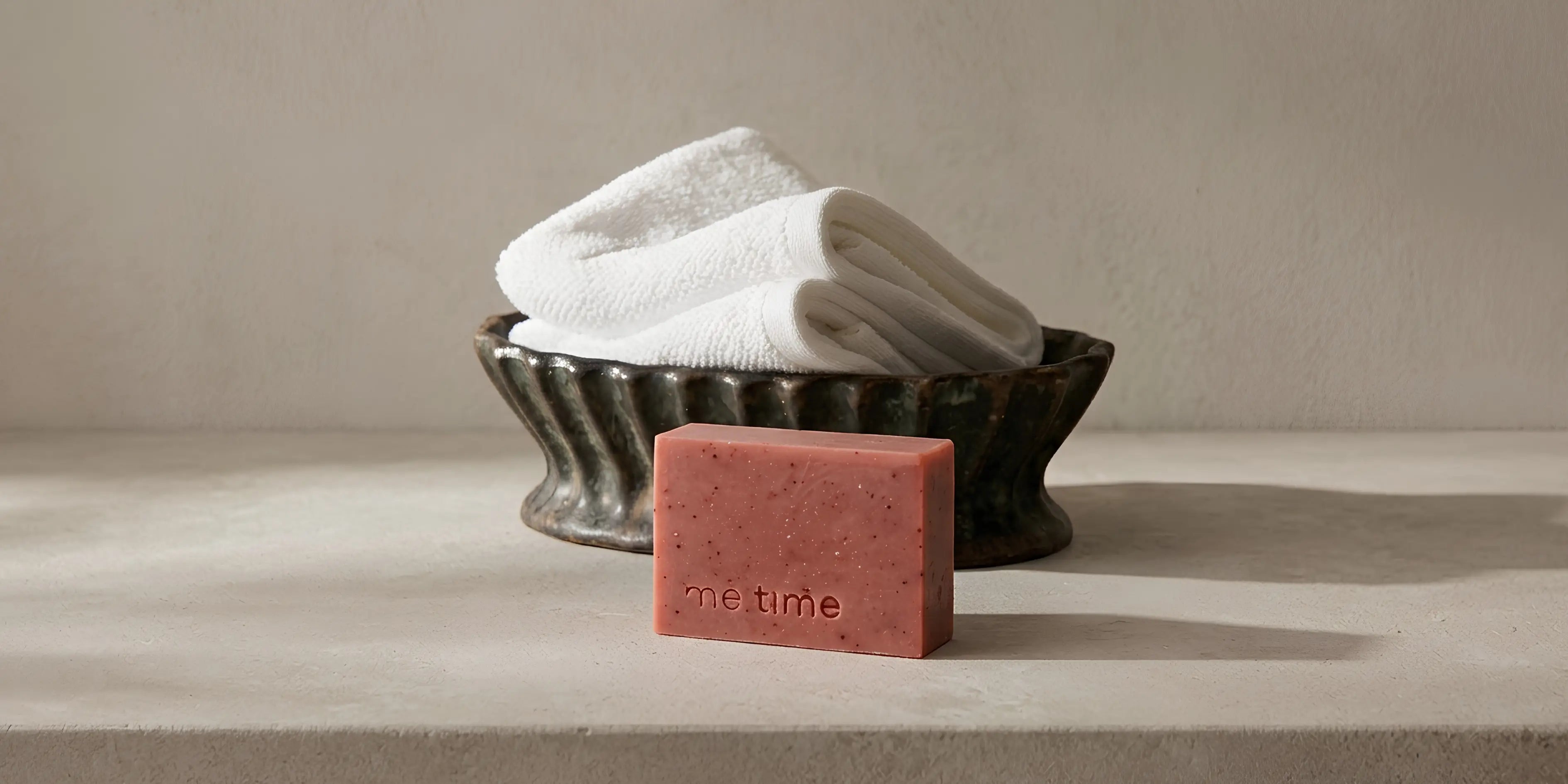 Bar of soap with 'one time' branding in front of folded towels on a neutral background