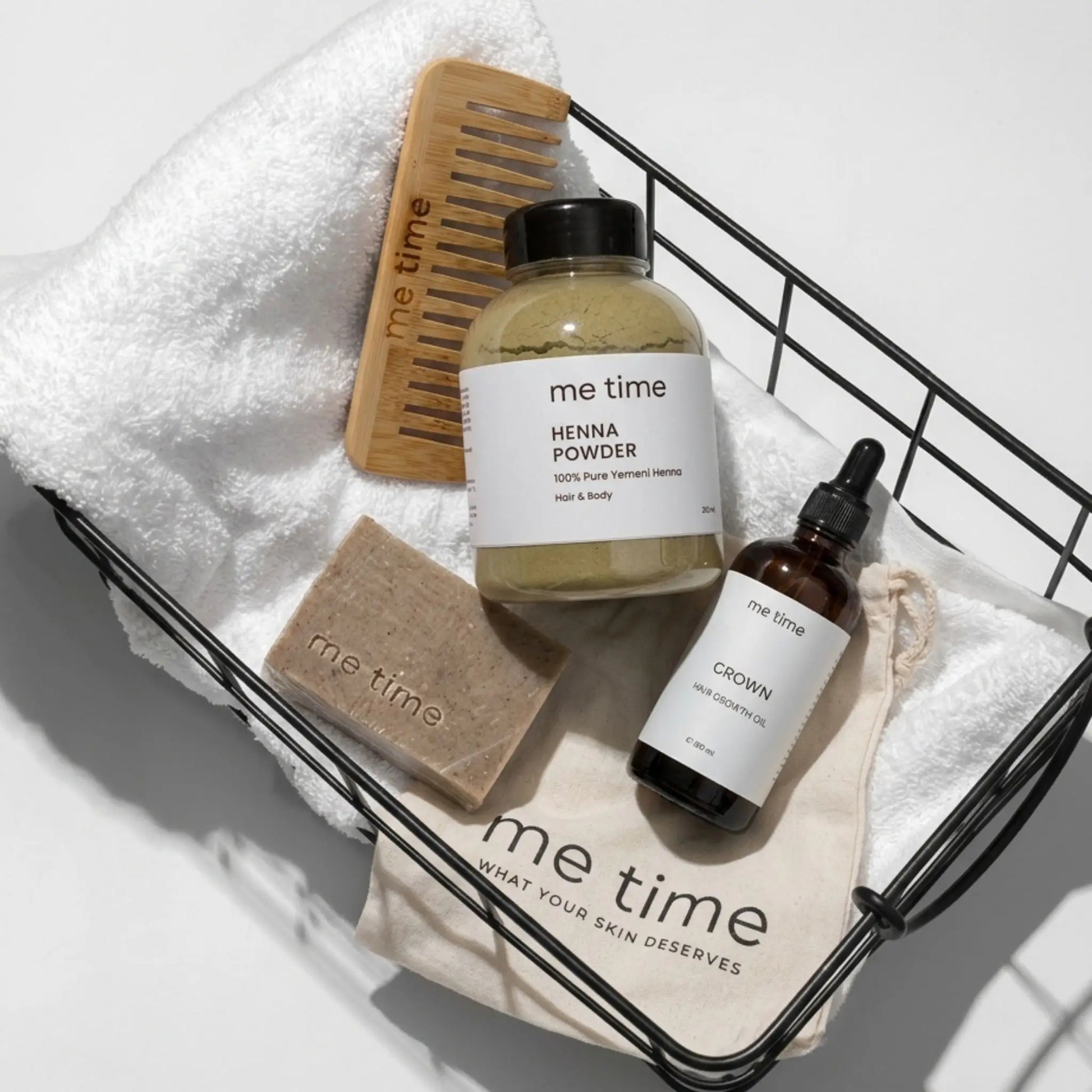 Hair Care Set from 'me time' products including henna powder, a comb, soap, and a bottle on a towel.