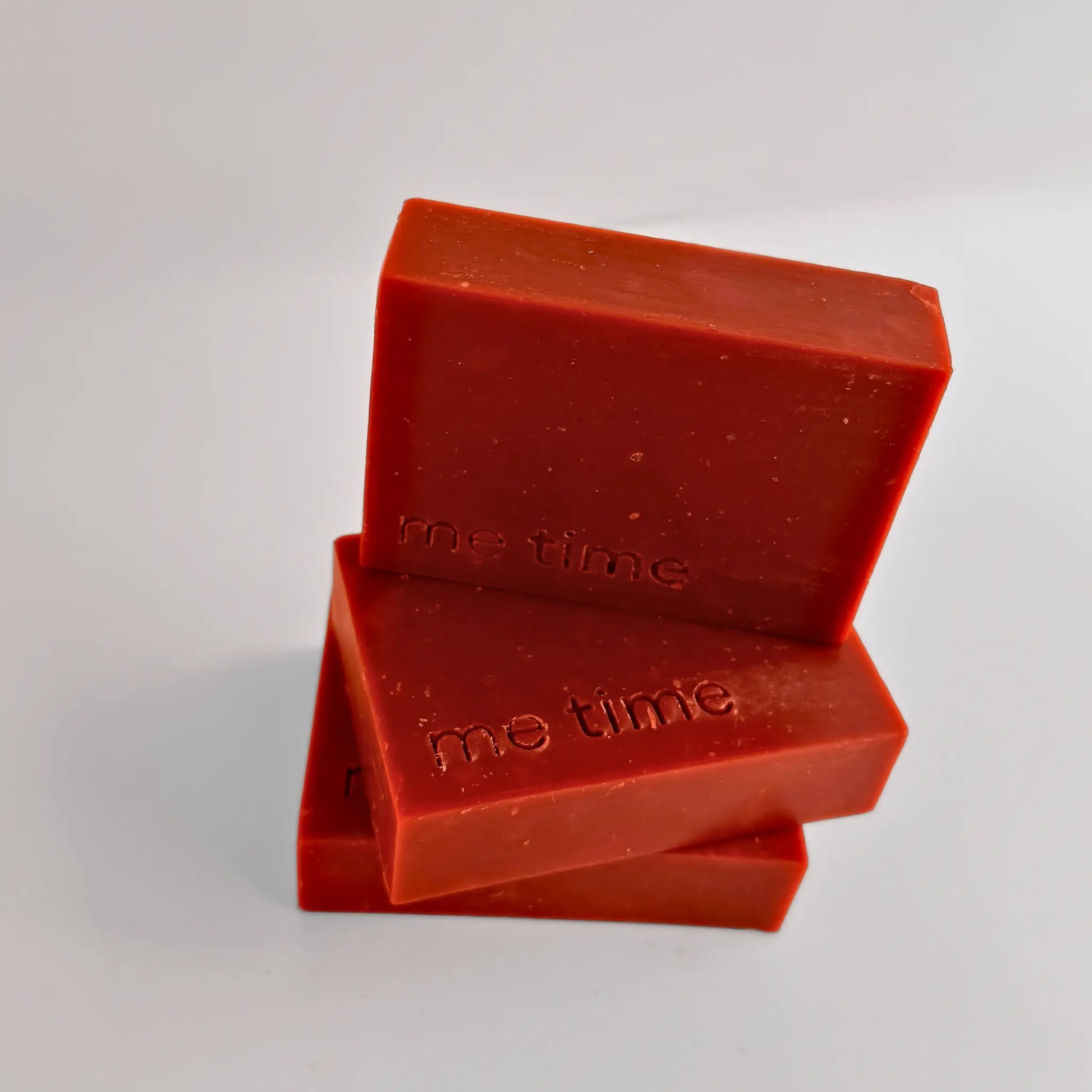 Three red bars of soap with 'me time' embossed on them, stacked on a light gray background.