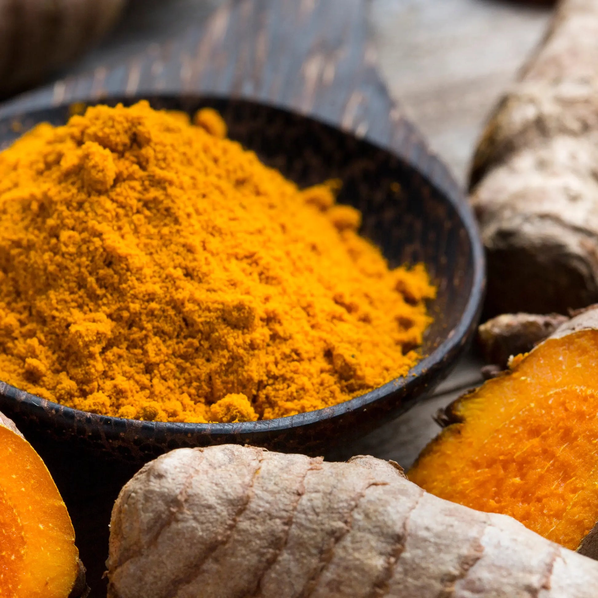 Turmeric powder in a black bowl with fresh turmeric roots on a wooden surface, me time soaps, UAE