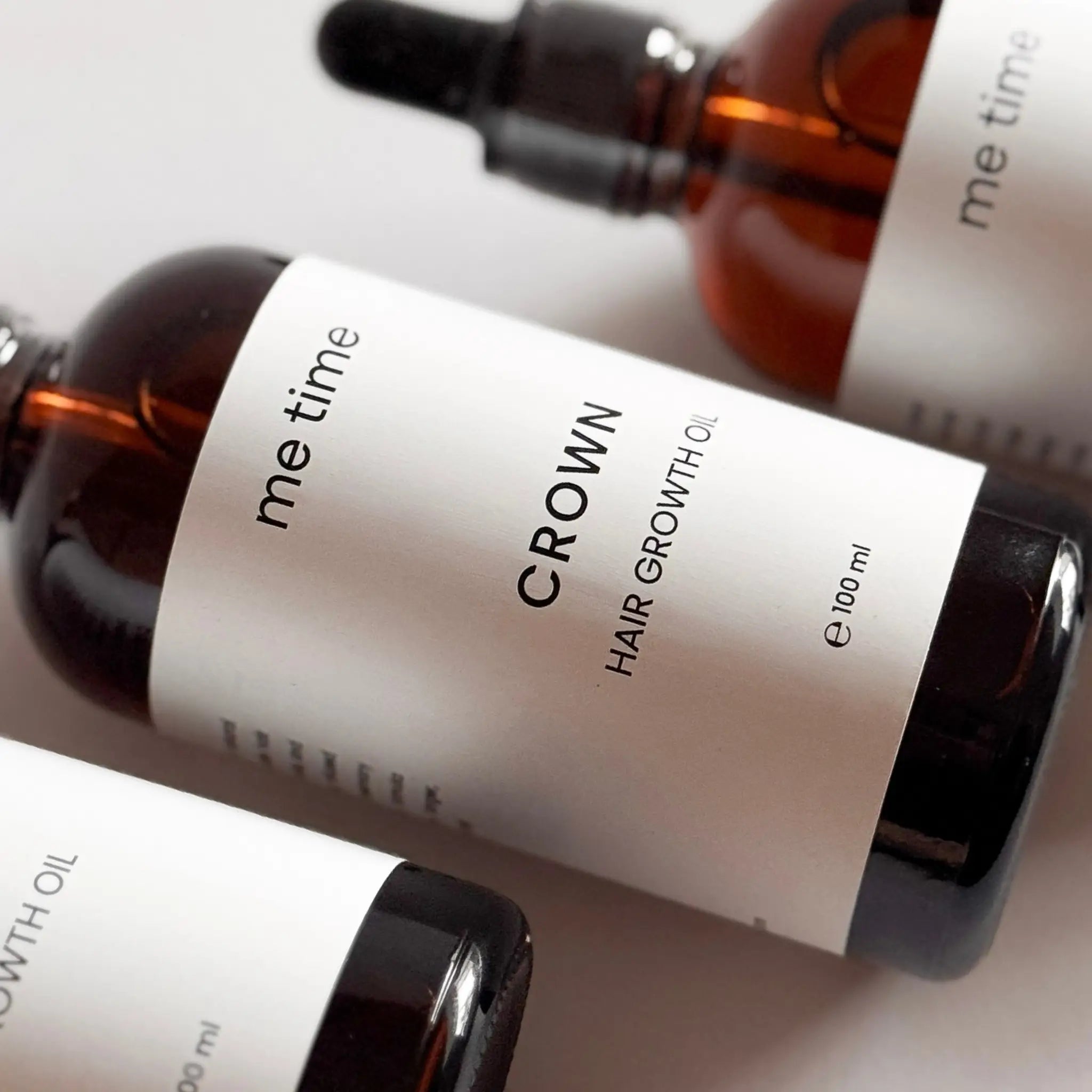 Bottle of Crown Hair Growth Oil with scattered natural ingredients like coconut, amla, and black seeds, neutral soft background, artisan premium style