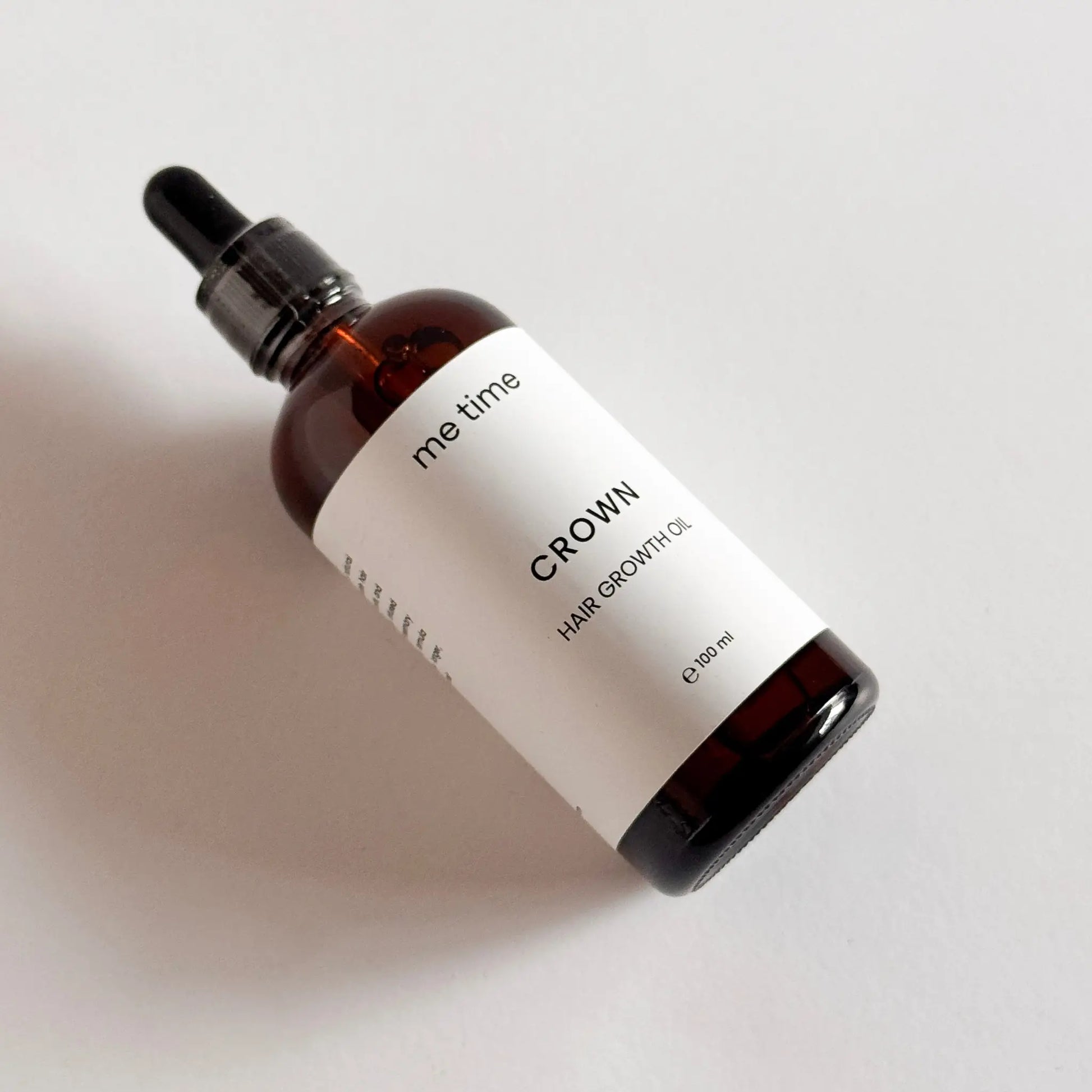 Elegant glass bottle of Crown Hair Growth Oil placed on a natural light grey surface, surrounded by fresh rosemary, black seeds, amla, and argan nuts, showcasing its premium natural ingredients for healthier, thicker hair.