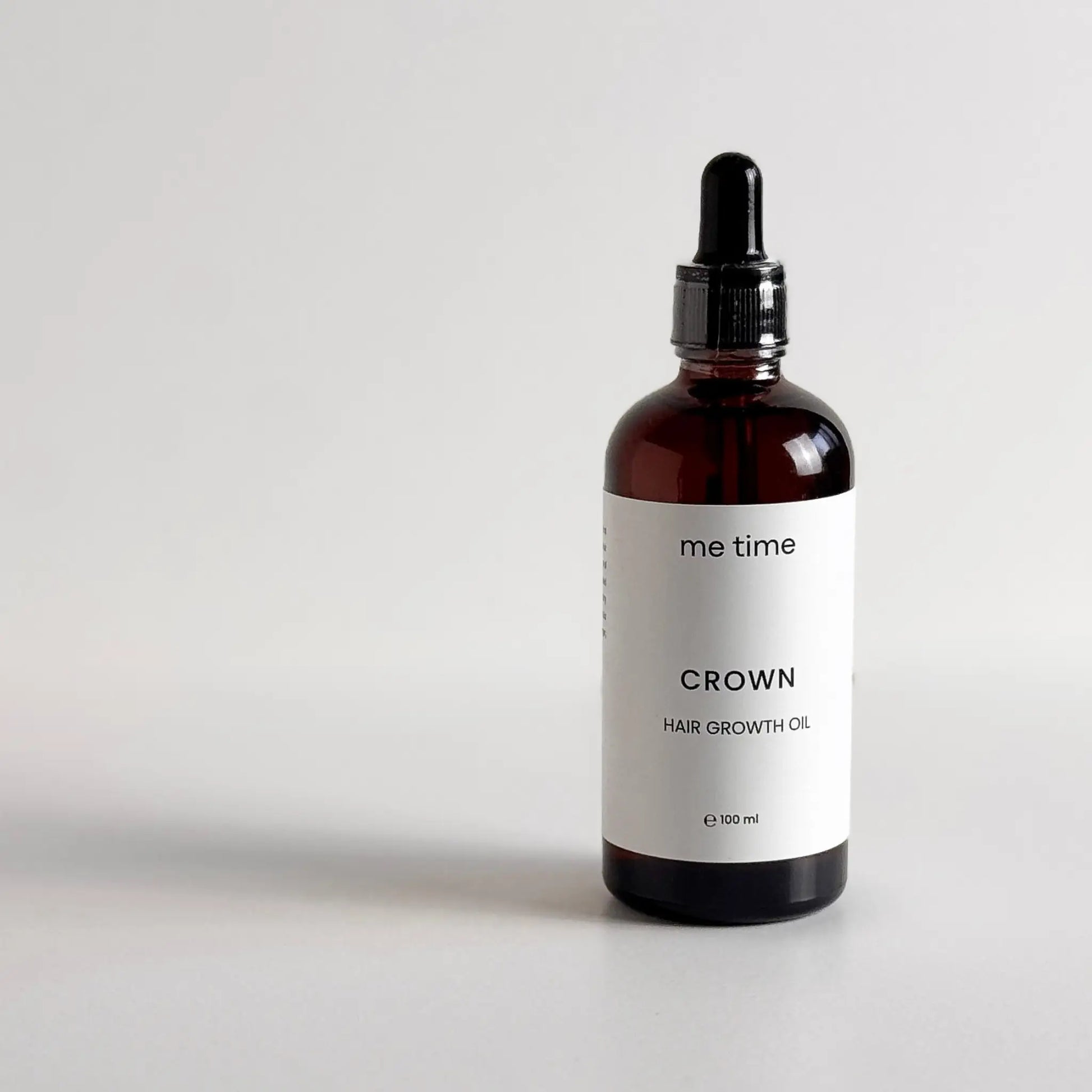 Elegant glass bottle of Crown Hair Growth Oil placed on a natural light grey surface, surrounded by fresh rosemary, black seeds, amla, and argan nuts, showcasing its premium natural ingredients for healthier, thicker hair.