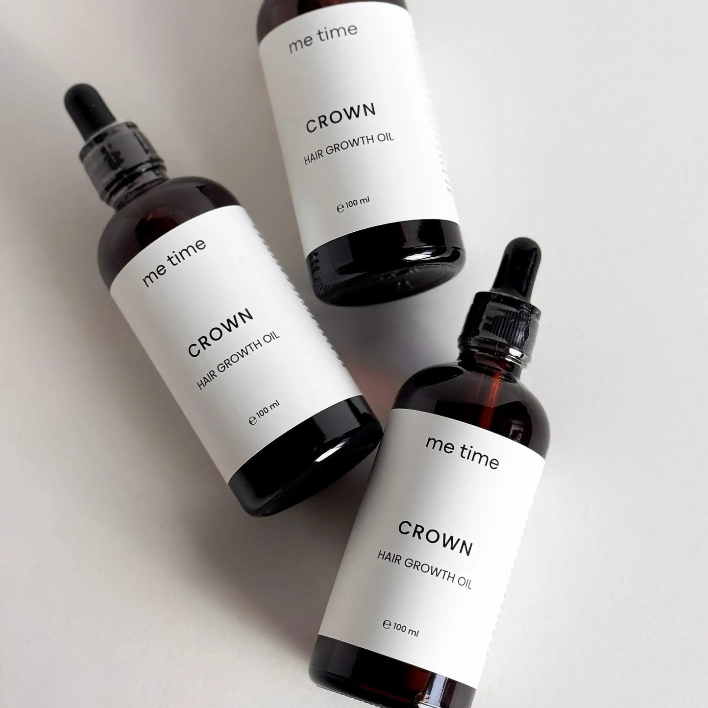 Elegant glass bottle of Crown Hair Growth Oil placed on a natural light grey surface, surrounded by fresh rosemary, black seeds, amla, and argan nuts, showcasing its premium natural ingredients for healthier, thicker hair.