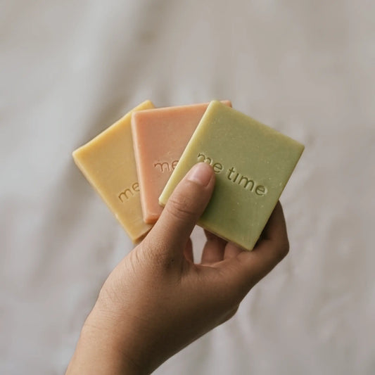Hand holding three bars of me time soap against a neutral background