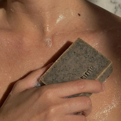 Hand holding a me time balck seed soap against skin