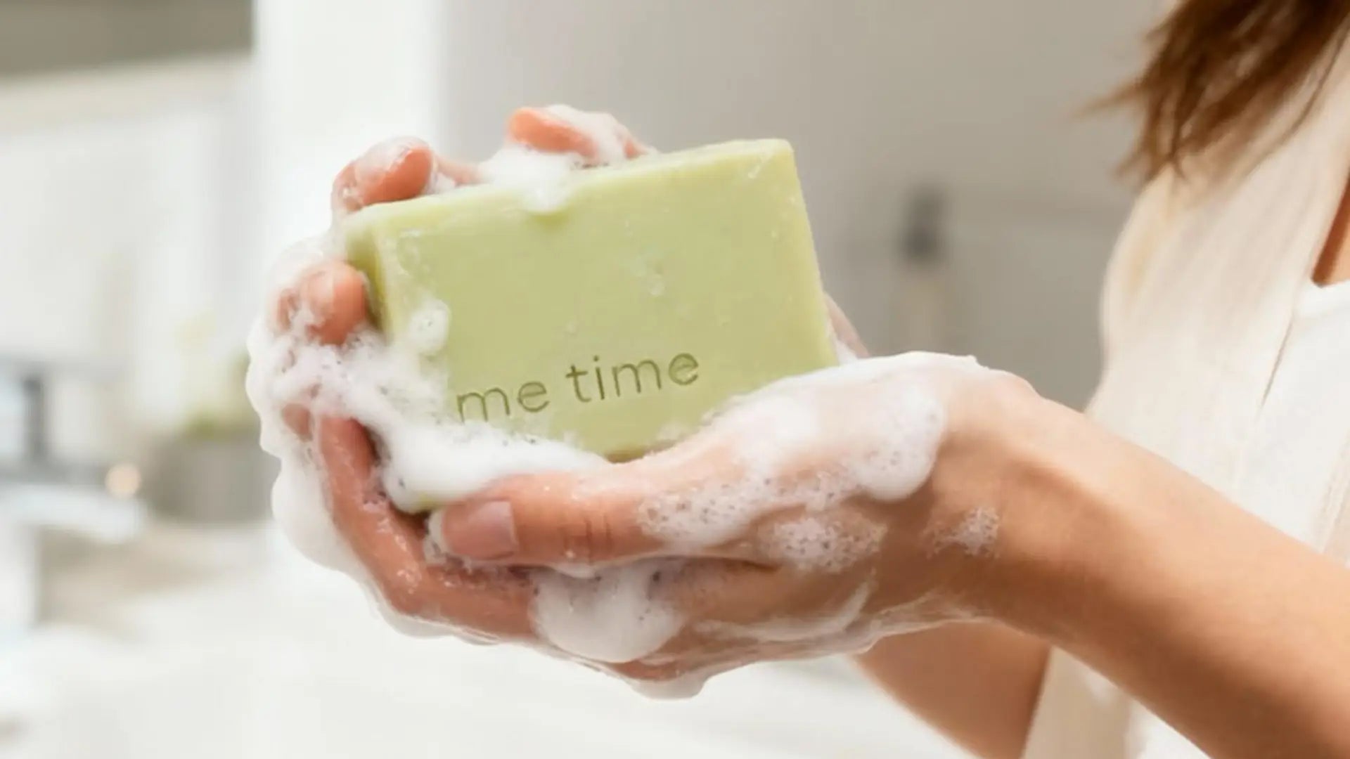 Person holding me time soap made in UAE, covered in foam, in a bathroom setting. 