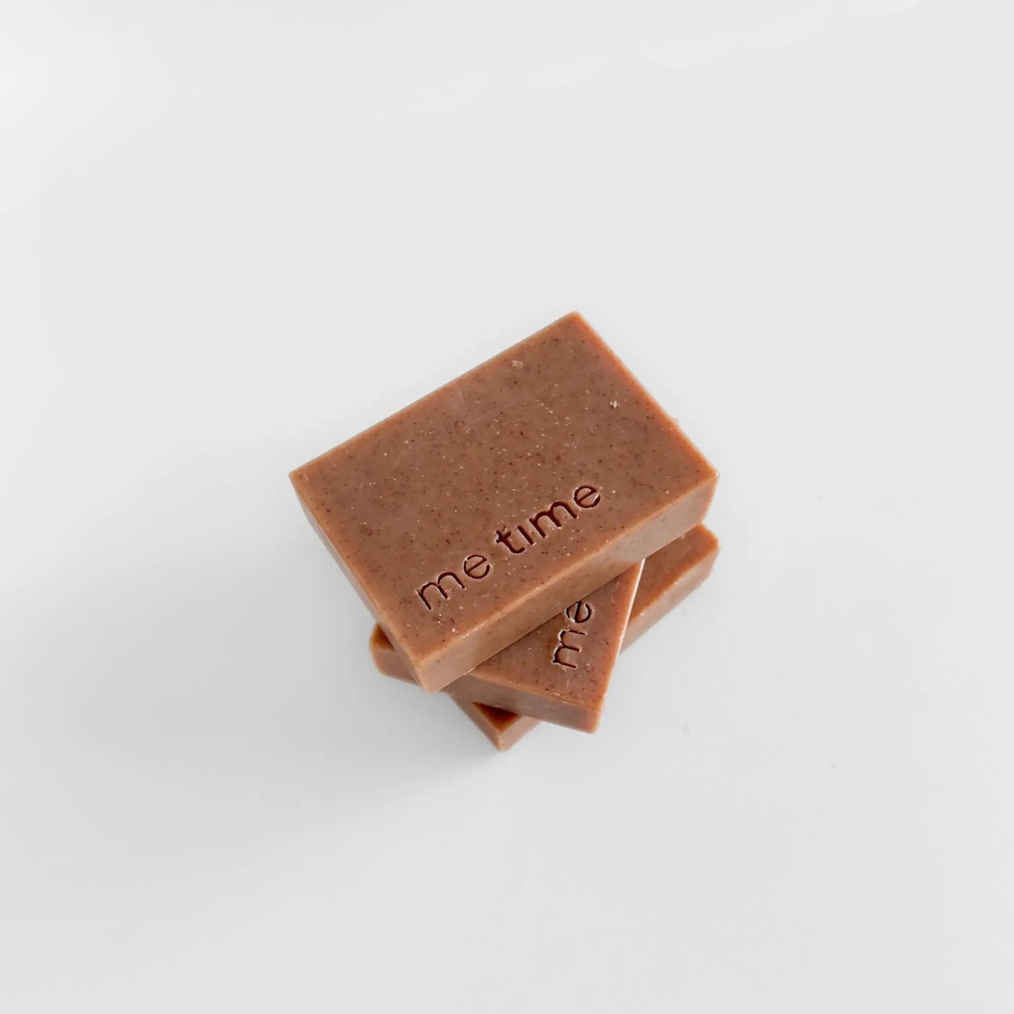 Two brown soap bars with 'me time' embossed on a light gray background